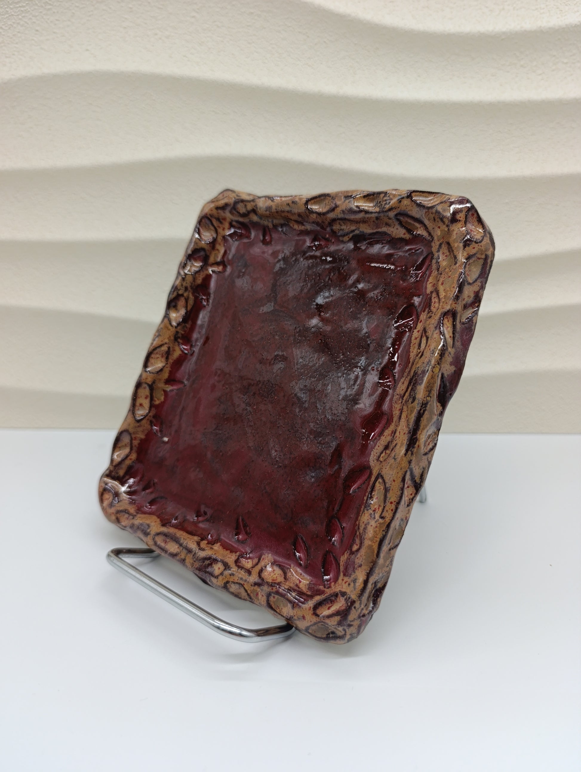 The Ember Frame Ceramic Tray combines rustic charm with timeless craftsmanship. Its rich red glaze, encased by a sculpted, fire-toned rim, gives it both warmth and character. Perfect for serving small bites, holding jewelry, or adding an artistic accent to your space, this handcrafted tray reflects the natural beauty and texture of clay shaped by hand and flame.