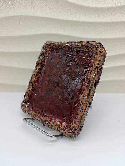 The Ember Frame Ceramic Tray combines rustic charm with timeless craftsmanship. Its rich red glaze, encased by a sculpted, fire-toned rim, gives it both warmth and character. Perfect for serving small bites, holding jewelry, or adding an artistic accent to your space, this handcrafted tray reflects the natural beauty and texture of clay shaped by hand and flame.