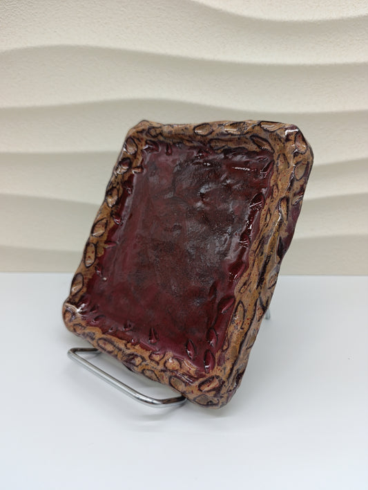 The Ember Frame Ceramic Tray combines rustic charm with timeless craftsmanship. Its rich red glaze, encased by a sculpted, fire-toned rim, gives it both warmth and character. Perfect for serving small bites, holding jewelry, or adding an artistic accent to your space, this handcrafted tray reflects the natural beauty and texture of clay shaped by hand and flame.