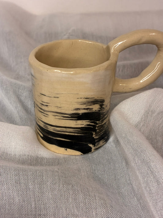 This cup looks like it got caught doodling during class — and we love it for that. Its smudgy black brush marks wrap around like windy scribbles on a beige canvas, giving it a cool, artsy, “I didn’t mean to look this good” attitude. With its chunky handle and quirky shape, the Scribble Sipster is ready for anyone who prefers their caffeine with a side of creative chaos.