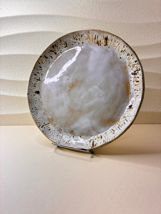 This handcrafted ceramic plate features a speckled glaze, creating a subtle, textured surface with natural variation. Each plate is individually made by hand, resulting in unique patterns that highlight its artisanal character. Designed exclusively for serving food