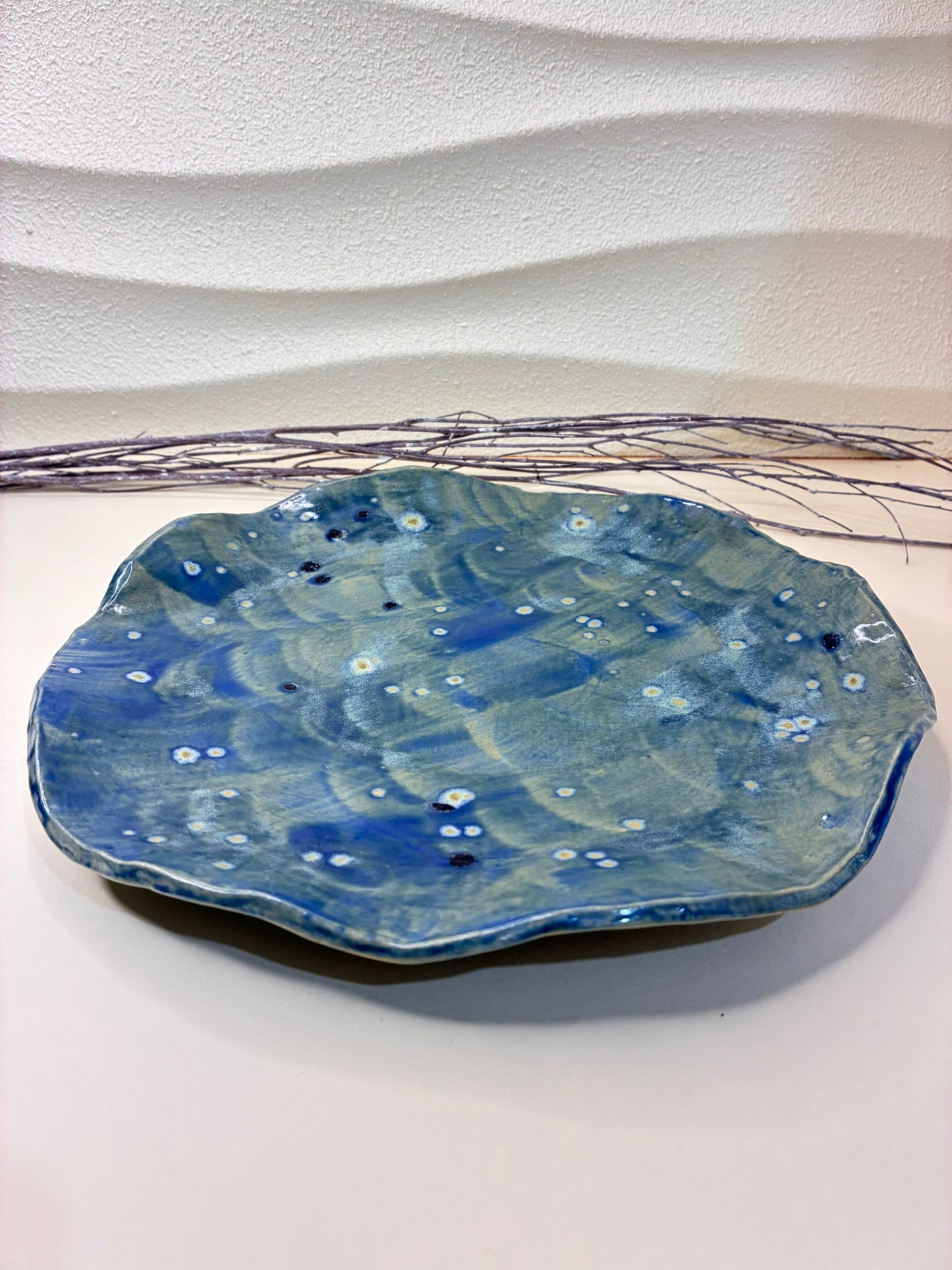 This handcrafted round plate features a blue glaze with subtle splashes, creating the effect of gentle waves across its surface. Each plate is unique, with organic variations in the glaze that highlight its artisanal character. Perfect for serving meals, it brings a sense of color, craftsmanship, and elegance to any dining table.