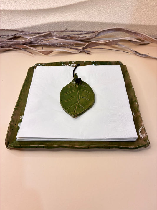 The Woodland Leaf Napkin Holder combines rustic charm with functional design. Handcrafted from speckled clay and finished with a glossy olive-green glaze, it features a square tray with a matching ceramic leaf weight to keep napkins neatly in place. The natural leaf motif evokes the tranquility of a forest table setting, making it a perfect accent for both everyday use and special gatherings. Elegant, earthy, and thoughtfully made — a beautiful fusion of art and utility.