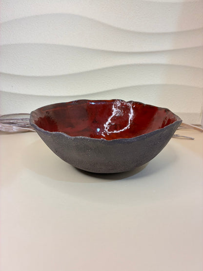 This bowl has a beautifully organic, handcrafted presence — a perfect balance between rugged earthiness and refined artistry.

Its outer surface is a deep, matte brown-black, textured like volcanic stone or dark clay. The form is slightly asymmetrical, with a softly undulating rim that gives it a natural, hand-formed character — embracing imperfection in a wabi-sabi sense.