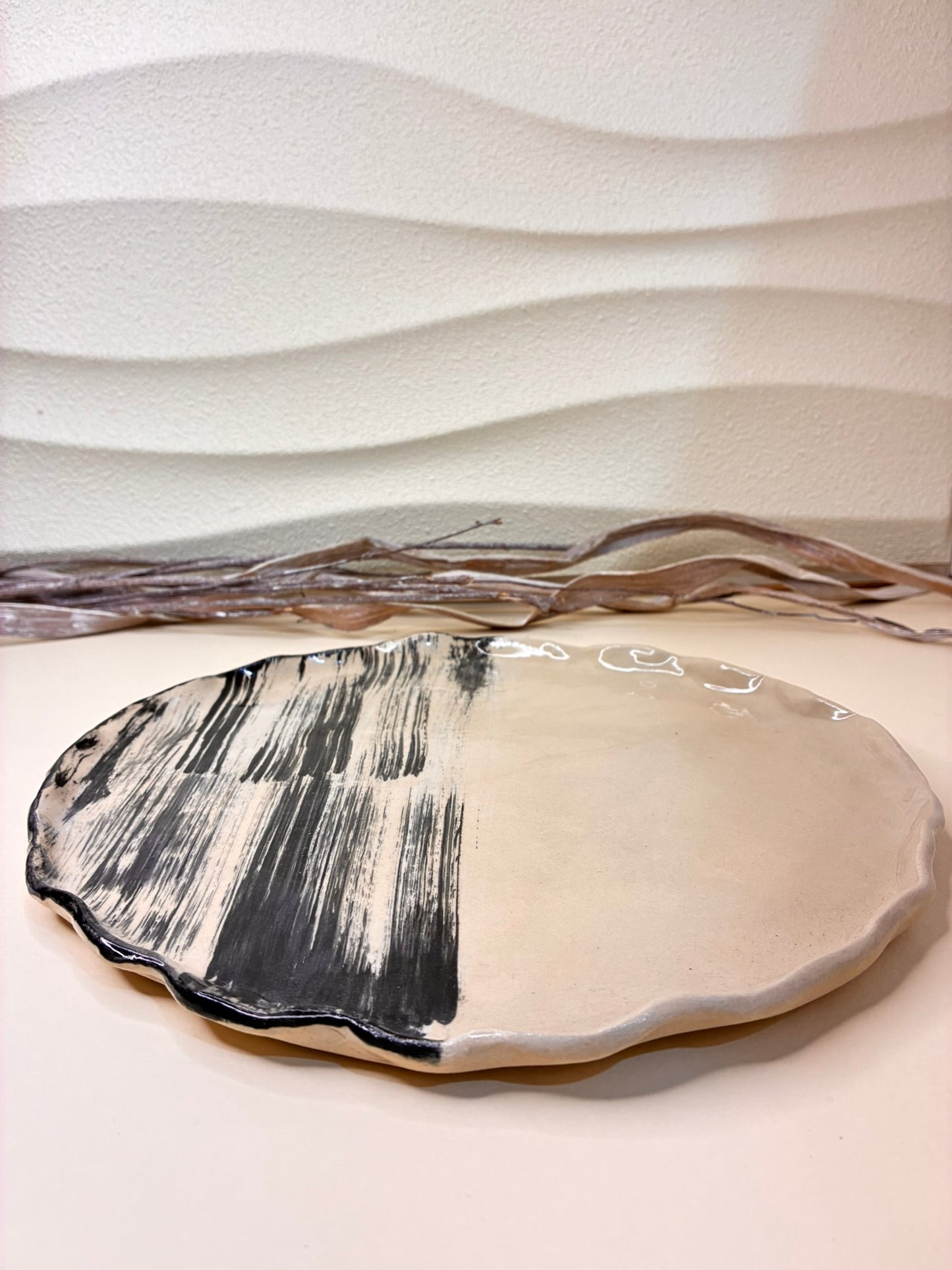 This handcrafted small ceramic plate features a wavy edge and hand-painted black-and-white brushstroke design, giving each piece a unique and artistic character. Part of a coordinated plate set, it complements the larger plate while adding texture and visual interest to the table. Perfectly suited for serving small dishes, appetizers, or desserts, it combines functional use with sculptural elegance, bringing a touch of artisanal craftsmanship to any dining setting.