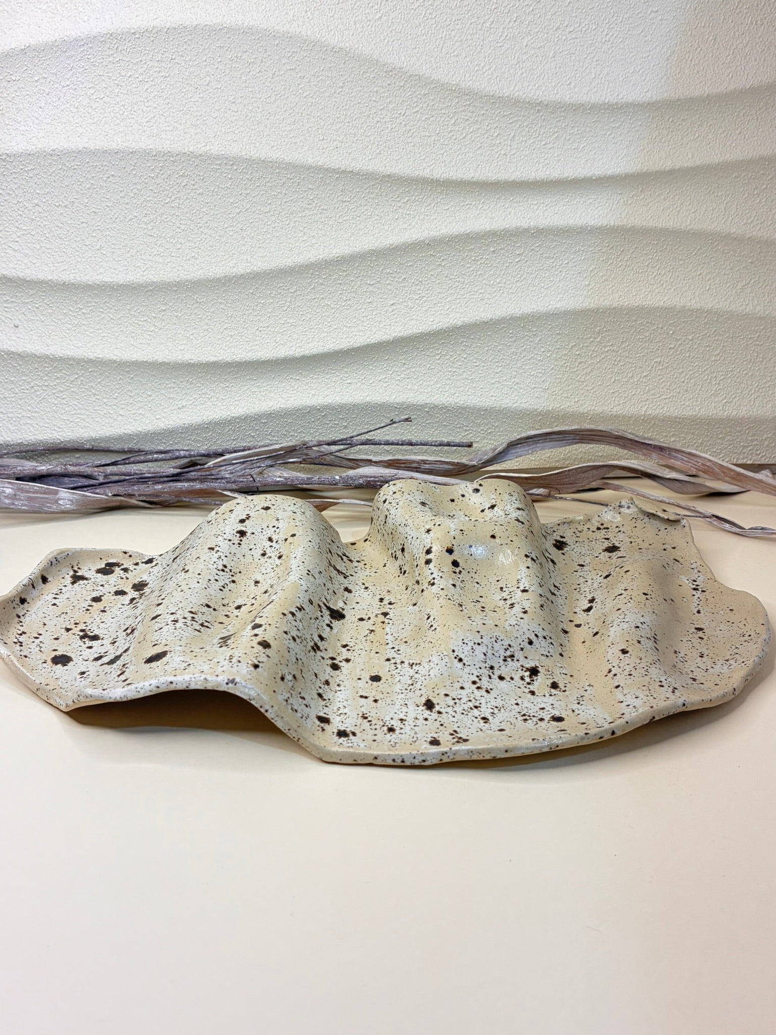 This handcrafted ceramic serving platter features a wavy, organic form and a winter wood–inspired color palette, blending soft neutral tones with natural depth and warmth. Its flowing edges and subtle surface variations highlight the handmade character of the piece. Designed for serving, it offers a refined yet earthy presence, making it ideal for presenting food with understated elegance.
