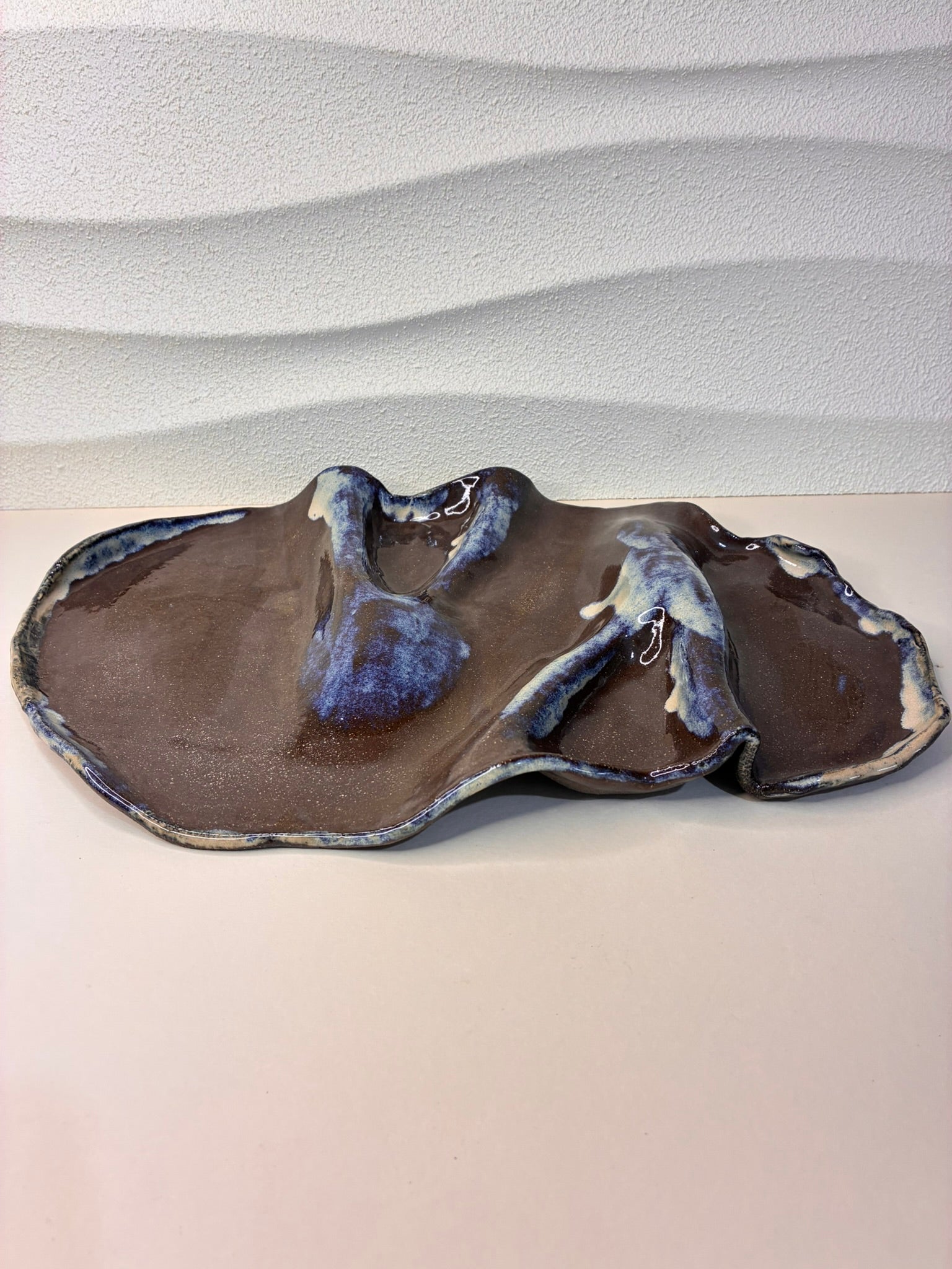 This handcrafted black stoneware platter features an organic glaze that appears to have naturally flowed across its surface, creating a unique, artistic texture. Perfect for serving cheeses, charcuterie, or small bites, it combines functionality with sculptural elegance. Each piece is individually made by hand, with subtle variations that highlight its artisanal character. A refined, minimalist design that brings a touch of modern sophistication to any tabletop or entertaining setting.