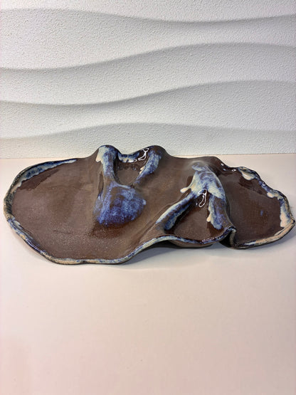 This handcrafted black stoneware platter features an organic glaze that appears to have naturally flowed across its surface, creating a unique, artistic texture. Perfect for serving cheeses, charcuterie, or small bites, it combines functionality with sculptural elegance. Each piece is individually made by hand, with subtle variations that highlight its artisanal character. A refined, minimalist design that brings a touch of modern sophistication to any tabletop or entertaining setting.