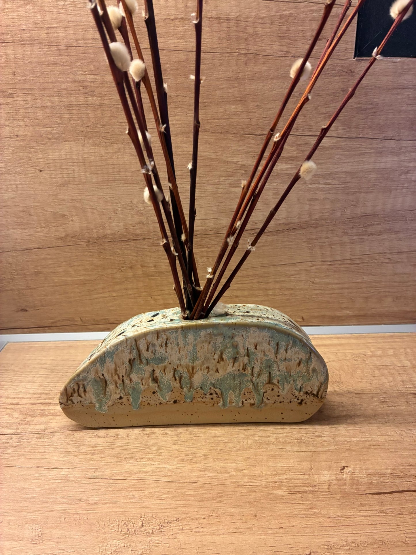 This handmade ceramic art object features a softly arched form inspired by coastal stone and eroded landscapes. Layered glazes in muted blue, sand, and earthy brown flow naturally across the surface, creating depth, texture, and movement. Each piece is one of a kind, shaped and fired by hand with organic variations that celebrate the ceramic process. Designed as a versatile sculptural object, it can be styled as a standalone art piece or used creatively as a vessel for dried botanicals , for fresh flowers ,