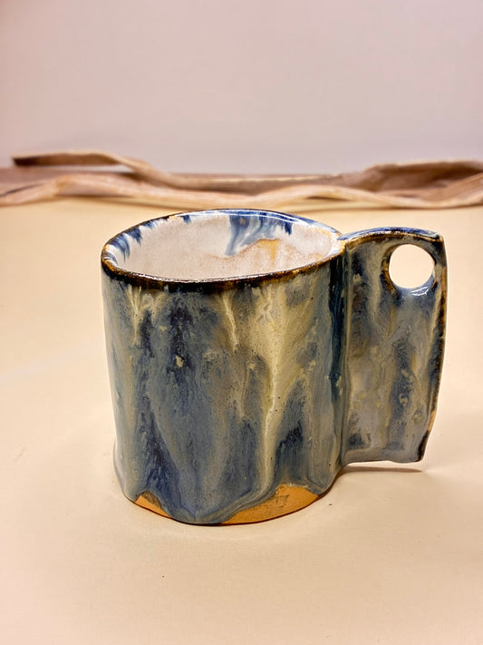 Handmade ceramic cup finished with a deep blue glaze and soft, drifting white lines that move gently across the surface. The flowing patterns are created naturally during the glazing process, making each cup unique. Calm and atmospheric, this piece evokes water, sky, and quiet movement—perfect for  coffee or tea moments.