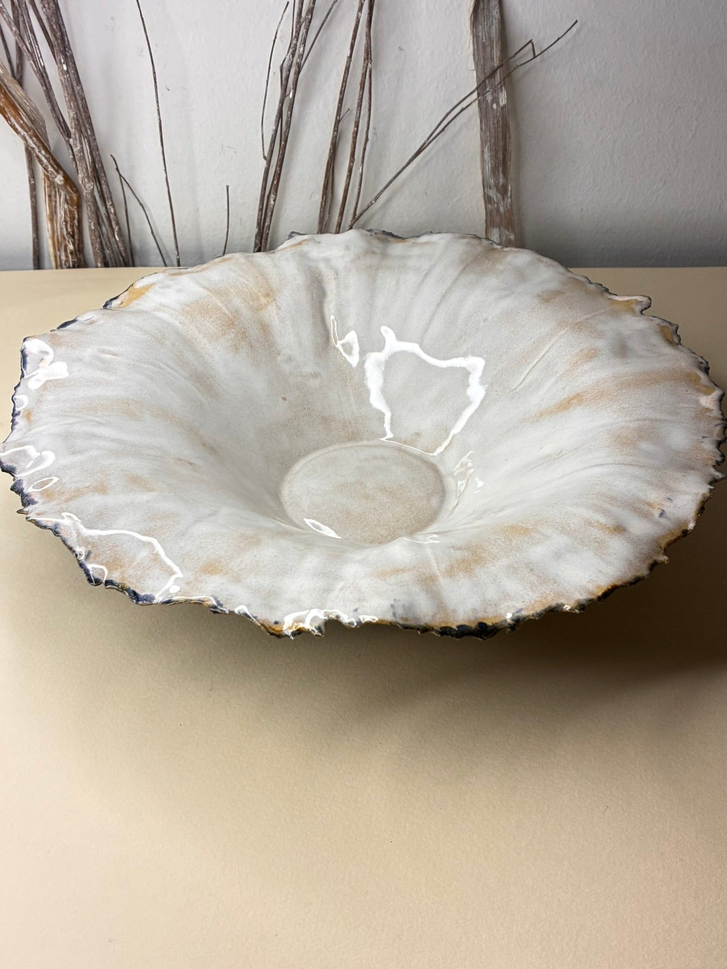 This handmade ceramic bowl is a unique, one-of-a-kind piece shaped with an organic, flowing rim inspired by natural forms. The interior features a soft ivory glaze with subtle warm tones, while the exterior contrasts beautifully with a dark, earthy finish speckled with natural variations—celebrating the character of handcrafted ceramics.