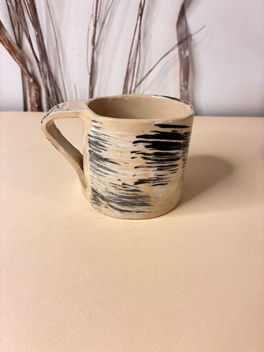 Handmade ceramic mug crafted from natural white clay and decorated with bold, expressive black brushstrokes. Each mark is applied by hand, creating subtle variations that make every piece unique. The strong contrast between the white clay and black strokes gives this mug a clean, modern character—an everyday object that feels like a small work of art.
