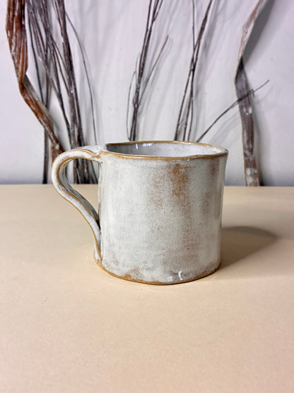 Handmade ceramic mug crafted from white clay with a soft, natural finish that subtly reveals the warm beige tones beneath the surface. The minimal design highlights the raw beauty of the material and the gentle variations created by hand shaping and firing. Calm, understated, and timeless, this mug is made for  coffee and tea moments.