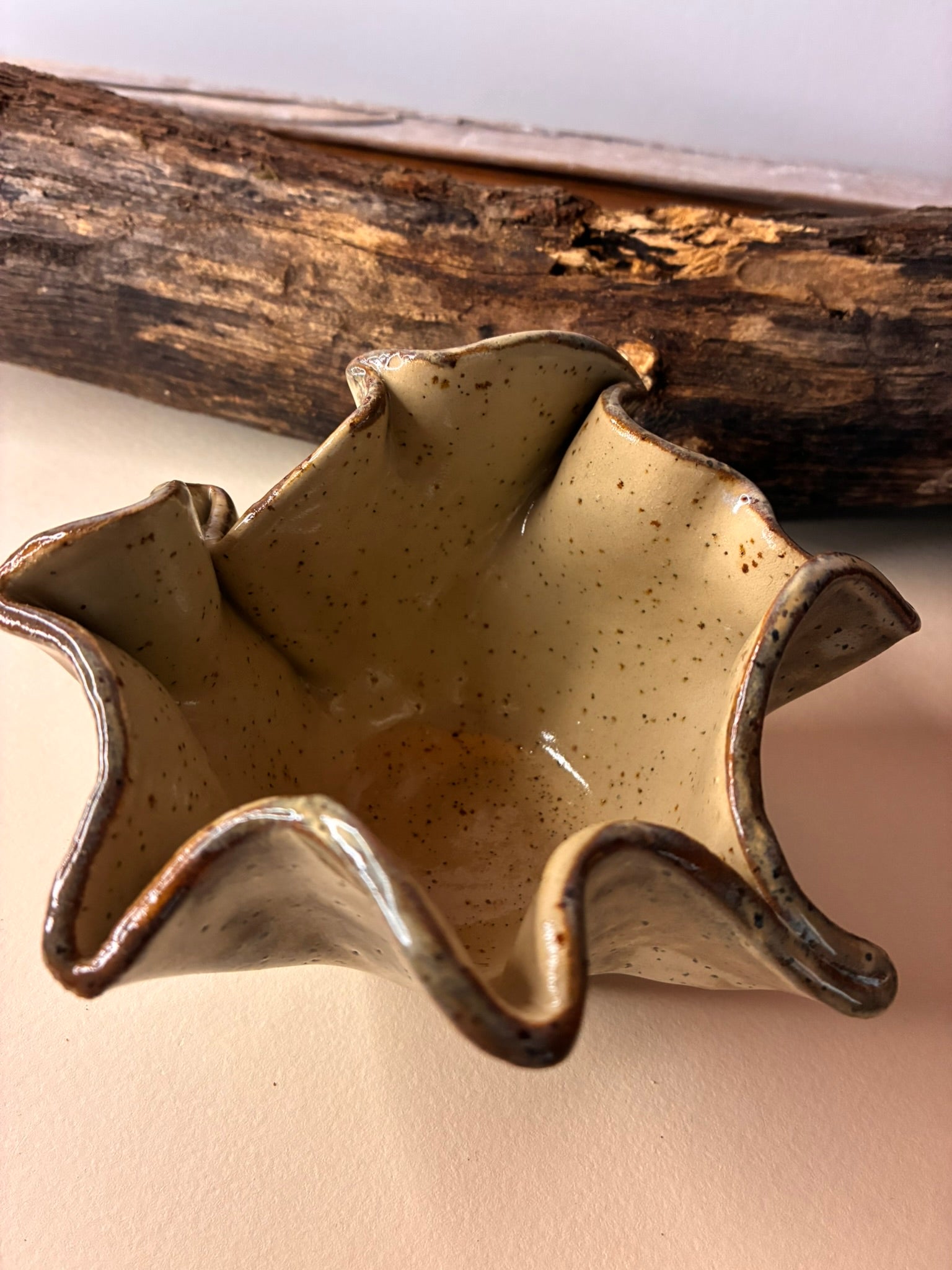 This handmade ceramic bowl features softly ruffled edges inspired by natural movement and imperfection. Finished in a warm, speckled glaze with subtle tonal variation, each piece is truly one of a kind. The organic shape makes it perfect as a catch-all for jewelry, a small serving bowl, or a sculptural accent for your home.